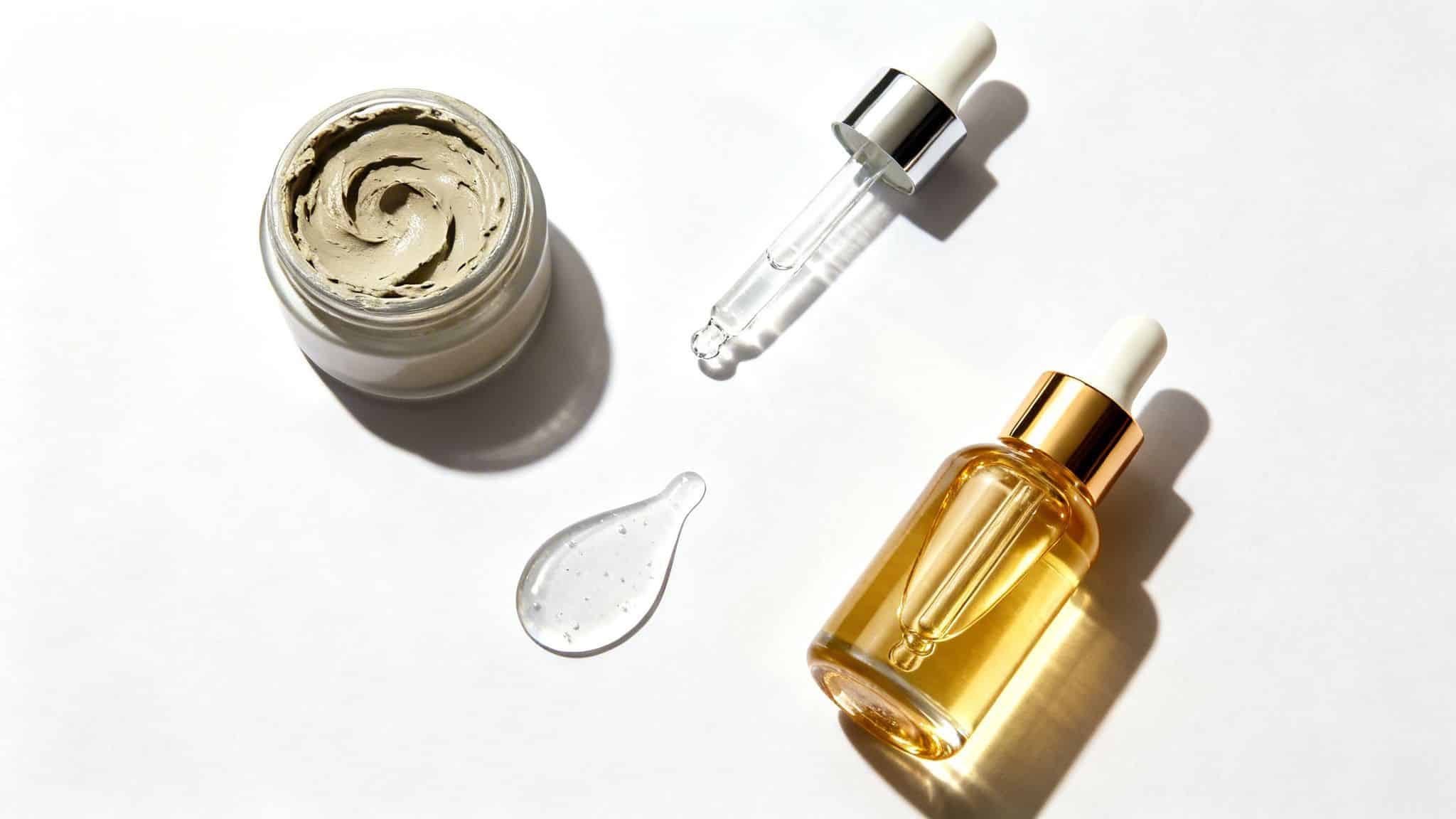 Divers produits de soins de la peau, dont un masque à l'argile, des sérums en flacons compte-gouttes et une goutte de gel transparent.