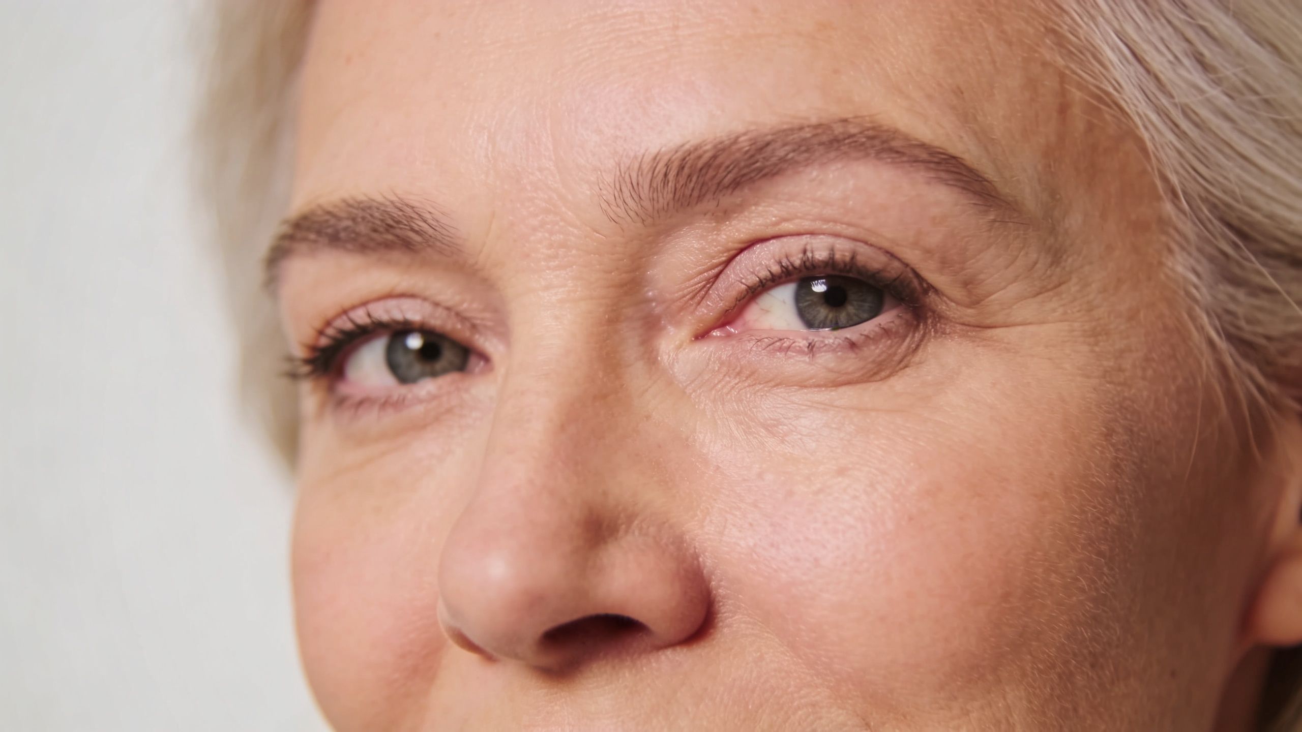 Gros plan sur le regard serein et les yeux d'une femme mature aux cheveux gris et naturels.