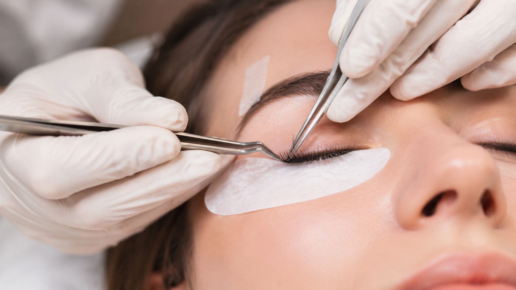 Une esthéticienne applique délicatement des extensions de cils sur une cliente à l'aide d'une pince professionnelle.
