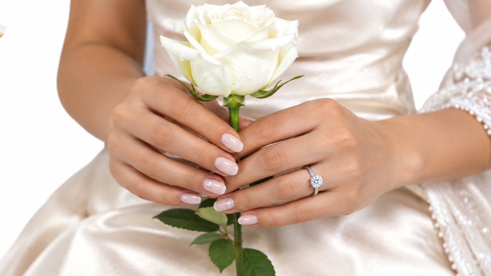 Une mariée élégante tenant une rose blanche, mettant en valeur ses ongles manucurés et sa bague de fiançailles.